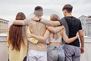 Four teenagers hug and stand with their backs on the roof of the house. Friends have a great time together photo