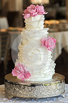 Four tier wedding cake with fondant ruffles and pink edible roses.