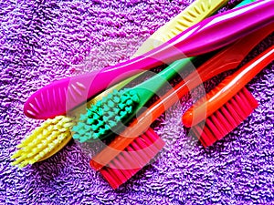 Four toothbrushes of various vivid colours laid on a purple towel.