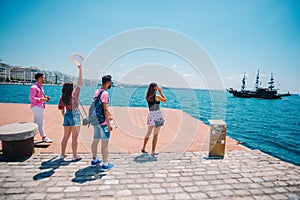 Four tourists waving at an old black pirate boat which is passing by next to a modern marine port