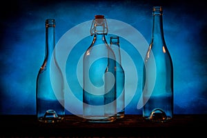 Four transparent glass bottles on a barn wood table in front of a blue background