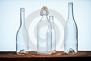 Four transparent glass bottles on a barn wood table in front of a white background