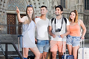 Four travelers holding map in hands and looking for their way in european town