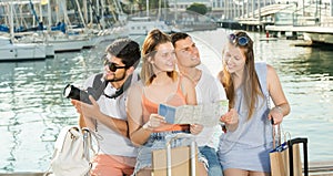 Four traveling young people searching for direction using paper map on waterfront in town