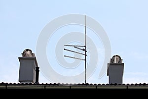 Four TV antennas mounted on strong metal pole on top of suburban family house roof next to two new modern chimneys