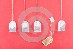 Four unused tea bags and one used tea bag isolated on red