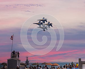 Four US Navy Blue Angels Jets flying in formation during sunset over a lifeguard stand at the beach during an airshow