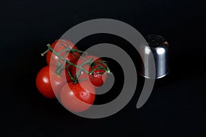 Four vine tomatos and salt shaker  on black background