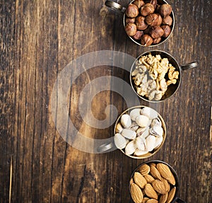 Four vintage cupro-nickel cup full of different nuts, almonds, pistachios, walnuts and hazelnuts on a dark wooden