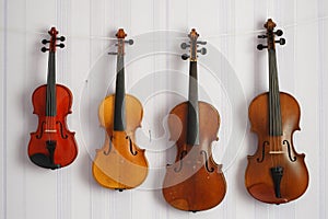 Four violins of a different sizes and colors hanging on the wall