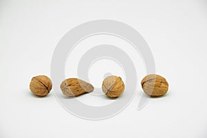 four walnuts in line on a white background in which one is a different walnut. Instead of being rounded it is elongated at the tip