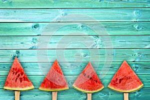 Four watermelon slice popsicles on blue wood background with copy space, summer fruit concept