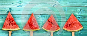 Four watermelon slice popsicles on panoramic blue wood background, fresh fruit concept