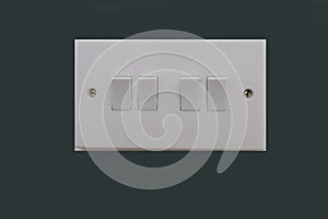 Four way electrical light switch.  White plastic switch with two screws, set against dark grey background