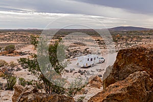 Four wheel drive vehicle and large white caravan camped beside a rocky outcrop.