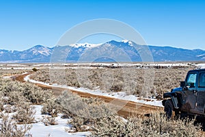 Four wheel drive vehicle on muddy dirt road curving towards snow-capped mountains