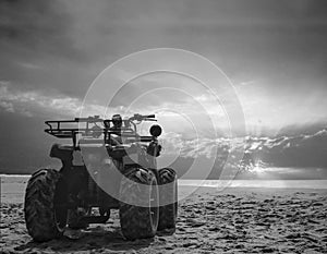 Four wheeler dirt bike on sand of sea beach during sunrise with dramatic colourful sky, black and white photo