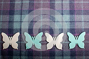 Four white and blue painted wood butterflies on light blue and grey textured textile wool material background with diagonal stripe