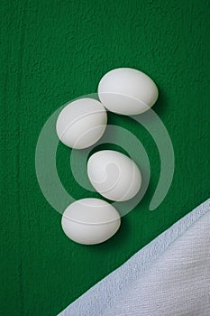 four white chicken eggs and a waffle dishcloth on green background