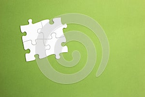 Four white jigsaw pieces fitted together to form a group joined on all sides. green background. copy space. working set. space for