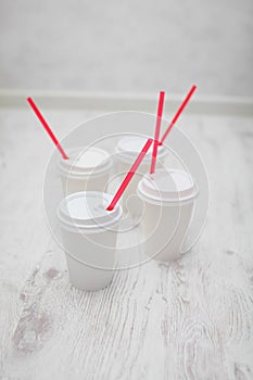 Four white paper cups with red tubes for coffee to go on white wooden table in selective focus