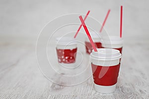 Four white paper cups with red tubes for coffee to go on white wooden table in selective focus