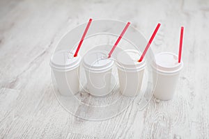Four white paper cups with red tubes for coffee to go on white wooden table in selective focus