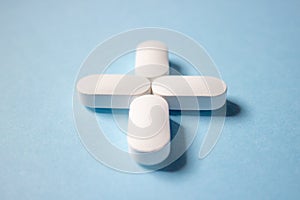 Four white pills are stacked in the form of a medical cross on a blue background