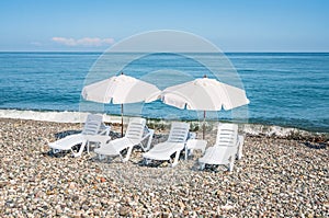 Four white plastic beach chairs and two white parasols on the be