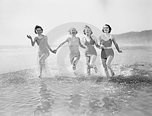 Vier Frauen laufen im wasser auf der Strand 