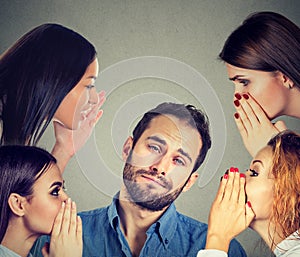 Four women whispering a secret gossip to a bored annoyed man
