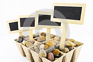 Four, wooden blank boards, label with stick, stuck in a cardboard extruder filled with decorative pebbles, conceptual photo,space