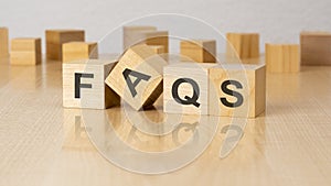four wooden blocks with text FAQS on table. copy space. white background.