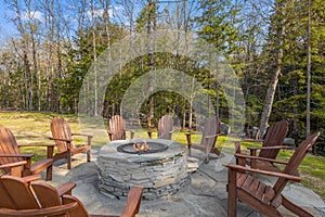 four wooden chairs surrounding a fire pit with stone and green grass in the foreground