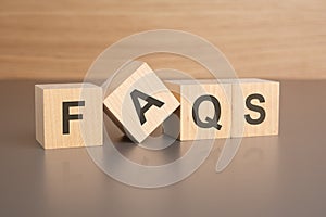 four wooden cubes with the letters FAQS on the bright surface of a brown table, business concept