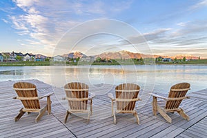 Four wooden lounge chairs facing the reflective Oquirrh Lake at Daybreak, Utah