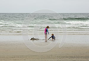 Two young children, a boy and a girl, playing in the sand and water at the beach
