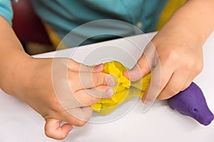 Four year old caucasian boy makes with hands animal figures from modeling yellow clay on white tabletop. Kids creativity preschool