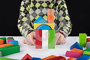 Four year old girl plays in the designer on the table. Wooden toys, colorful children`s designer, black background, entertainment