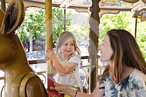 Little girl in carousel smiling and looking at mother photo