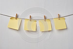 Four yellow blank notes hanging on the rope on white wooden background