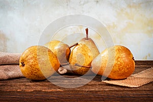 Four yellow pears and a fern on a barn wood table in front of a backdrop
