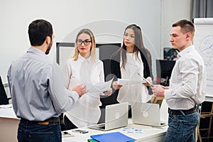 Four young business people working as a team gathered around laptop computer in an open plan modern office