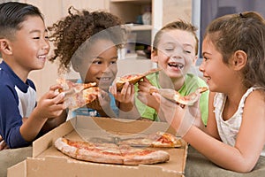 Four young children indoors eating pizza photo