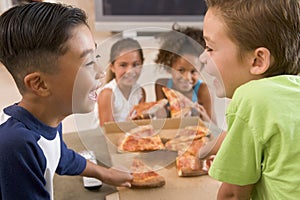 Four young children indoors eating pizza