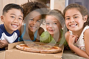 Four young children indoors with pizza smiling