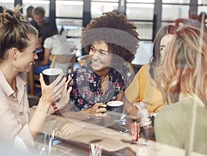 Four Young Female Friends Meeting Sit At Table In Coffee Shop And Talk