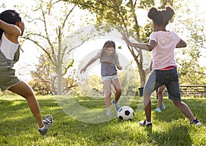 Four young girlfriends kicking football together in a park