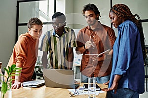 Four young intercultural creative designers looking at laptop screen