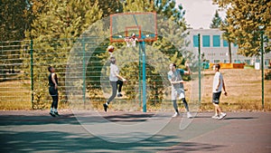 Four young men playing basketball on the sports ground outdoors